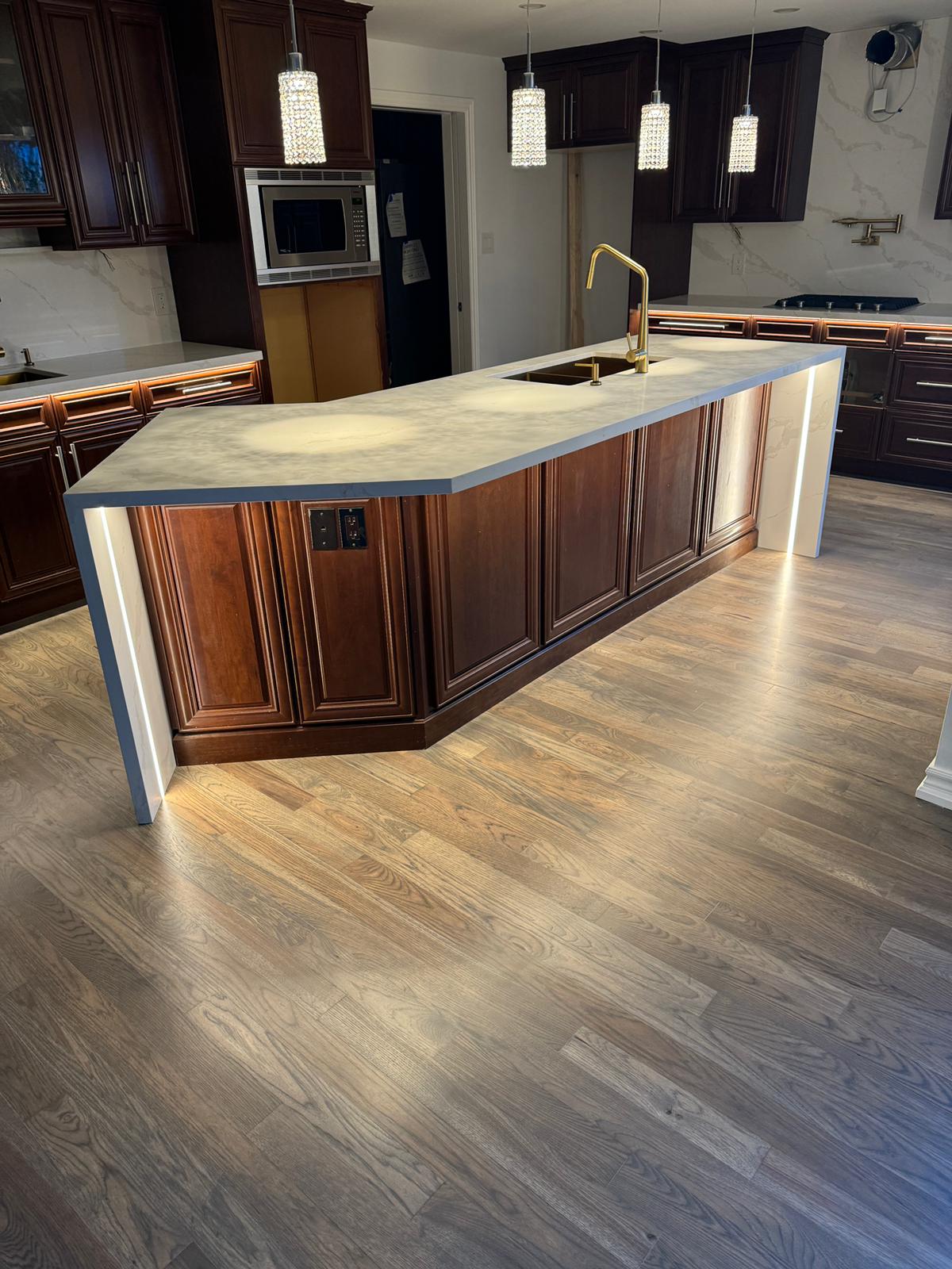 Elegant kitchen featuring a Calacatta quartz waterfall island with underglow LED lighting, rich dark wood cabinetry, gold fixtures, and modern pendant lighting.