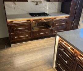Elegant kitchen featuring dark wood cabinetry with underglow lighting, Calacatta quartz countertops and backsplash, modern stainless steel hardware, and a built-in cooktop with a gold pot filler.