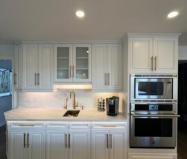 Elegant white kitchen featuring quartz countertops and backsplash, gold fixtures, glass-paneled cabinetry, built-in microwave and oven, and a stylish undermount sink.