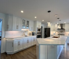 Bright and modern white kitchen featuring a large quartz waterfall island with mitered edges, gold hardware, custom cabinetry, and elegant pendant lighting.