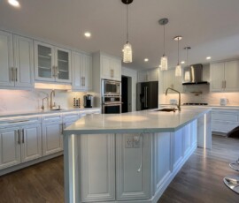 Spacious white kitchen featuring an oversized quartz waterfall island with mitered edges, gold hardware, custom cabinetry, built-in appliances, and elegant pendant lighting.