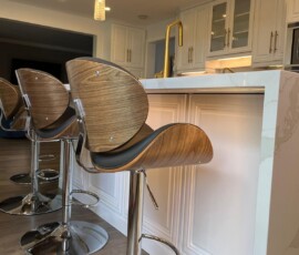 Stylish kitchen island featuring a quartz waterfall leg with a sleek miter edge, complemented by wood and chrome bar stools, gold fixtures, and pendant lighting.
