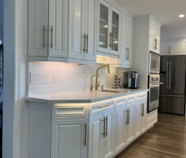 Stylish white kitchen featuring quartz countertops, gold hardware, glass-paneled cabinets, and a modern gold faucet, complemented by warm wood flooring.