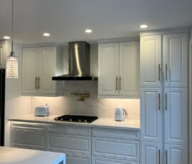Luxury white kitchen featuring sleek quartz countertops, matching backsplash, custom cabinetry, and a stainless steel range hood.