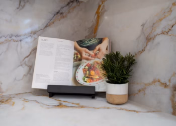 Close-up of Calacatta Aurora Gold Quartz countertop and backsplash with gold veining, styled with a recipe book and small potted plant.