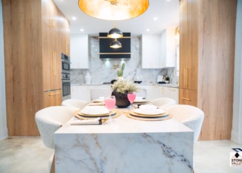 Front view of a Calacatta Aurora Gold Quartz dining table with bold gold veining, styled with modern place settings and overlooking a luxury kitchen with matching quartz surfaces.