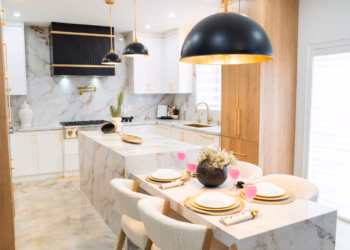 Open-concept kitchen showcasing a Calacatta Aurora Gold Quartz island and dining table with striking gold veining, paired with modern lighting, wood cabinetry, and white seating.