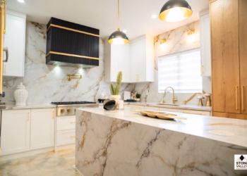 Luxury kitchen featuring Calacatta Aurora Gold Quartz countertops and full-height backsplash with bold gold veining, complemented by white cabinetry, gold fixtures, and a waterfall island.