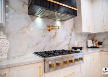 Close-up of Calacatta Aurora Gold Quartz backsplash and countertops with bold gold veining behind a stainless steel stove and modern gold pot filler.