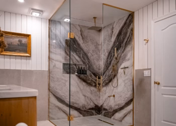 Luxury bathroom featuring Lyra quartz bookmatched shower walls with gold fixtures and glass enclosure.