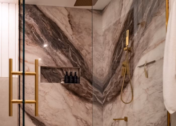 Entrance view of a luxury shower featuring book matched Lyra quartz walls, gold hardware, and a glass enclosure.