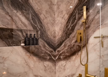 Closeup of Lyra quartz book matched shower walls with dramatic veining and gold fixtures.