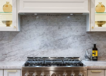 Taj Mahal Quartz countertops with warm veining in a bright white kitchen featuring a stainless-steel sink, gold faucet, and matching gold hardware.