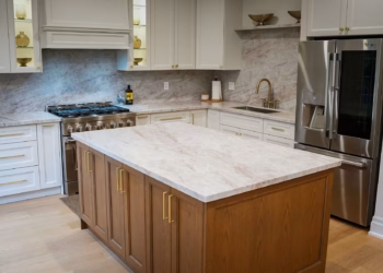 Taj Mahal Quartz kitchen with warm veining, a full-height backsplash, white cabinets, and brass hardware.