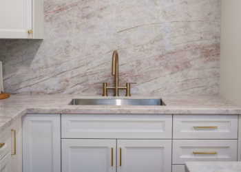 Taj Mahal Quartz countertops and full-height backsplash in a luxury kitchen with white cabinets, brass hardware, and a natural wood island.