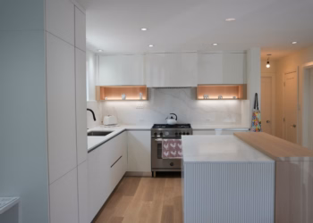 Modern kitchen featuring Calacatta Oro Quartz countertops and full-height backsplash, a half-quartz half–butcher block island, white cabinetry, and warm wood accents around the stove area.