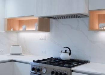 Calacatta Oro Quartz backsplash and countertops surrounding a modern gas stove with white cabinetry and warm wood accents, installed by Stone Valley Countertops.