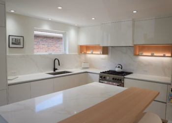 Kitchen with Calacatta Oro quartz backsplash and countertop behind a gas range, paired with a half quartz, half butcher block island featuring elegant gold veining and white cabinetry.